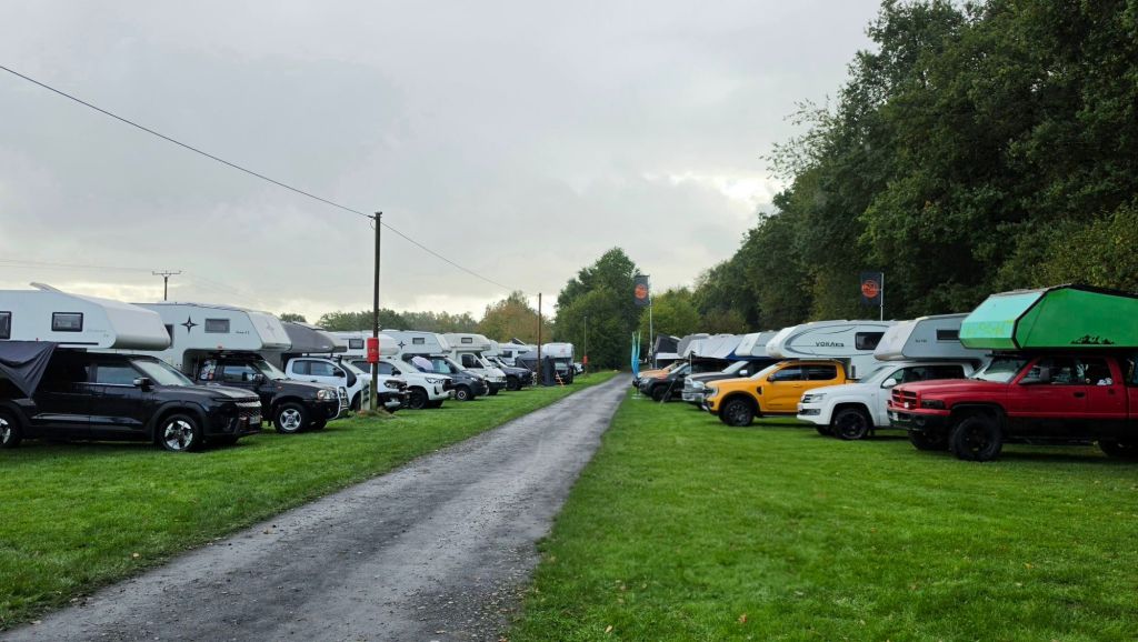 Eine Reihe von Wohnmobilen und Geländewagen entlang eines geschotterten Weges in einer grünen Umgebung.