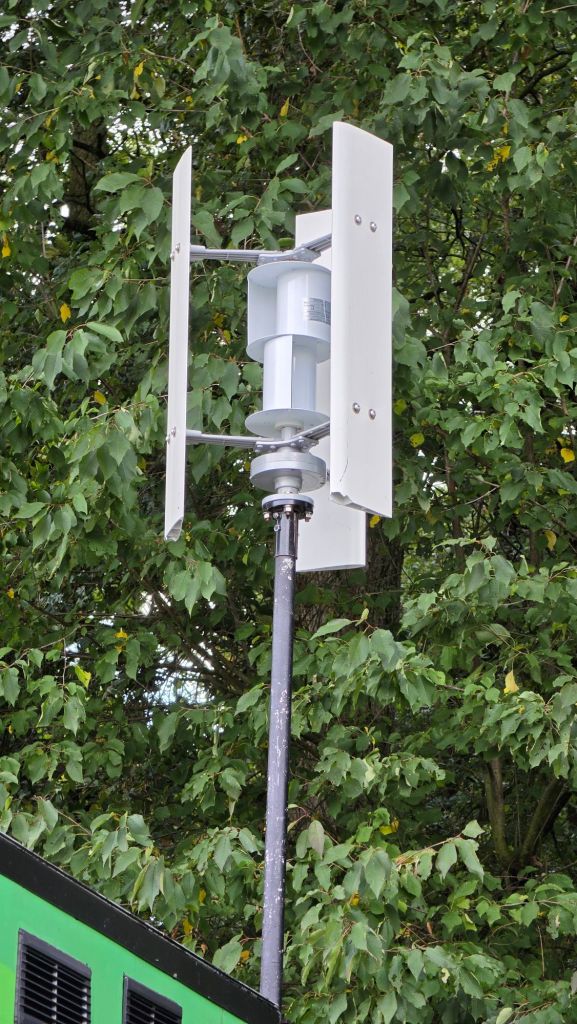 Ein Wetterstation-Sensor auf einem Mast, umgeben von grünen Blättern.