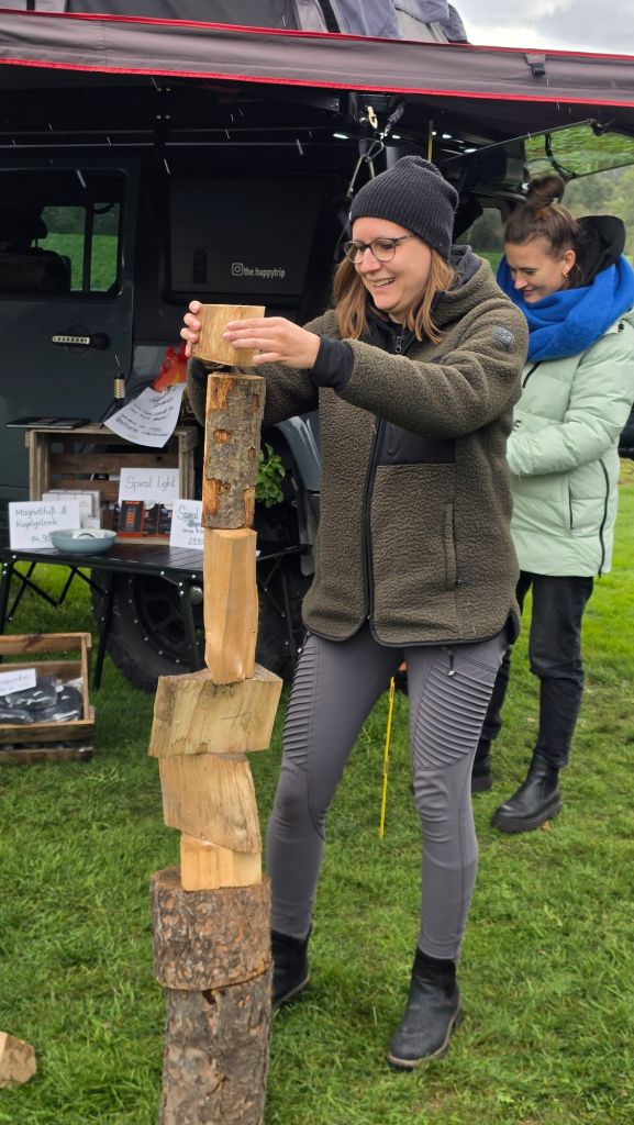 Eine Frau lächelt und stapelt Holzstücke an einem Verkaufsstand im Freien.