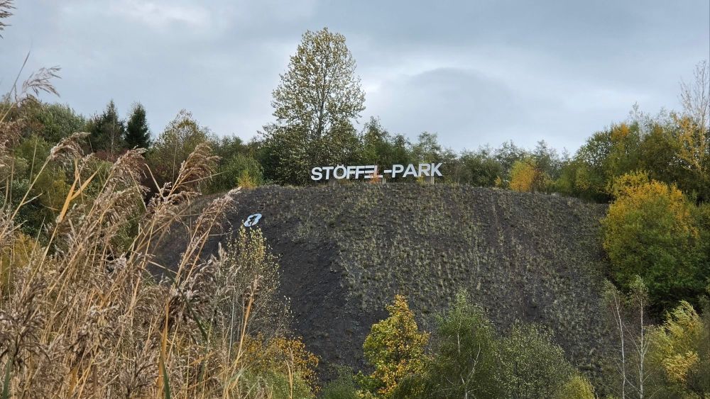 Ein Aussichtspunkt mit dem Schriftzug 'STÖFFEL-PARK' auf einer Hügelkuppe, umgeben von Bäumen und Grünbewuchs.