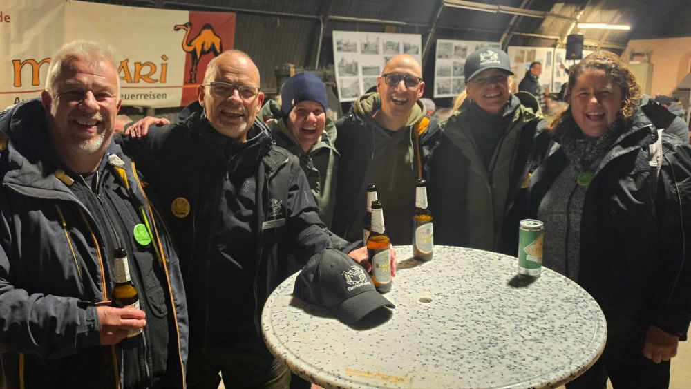 Gruppe von sechs Personen, die zusammen an einem Stehtisch stehen, mit Getränken in der Hand, lächeln und freuen sich.