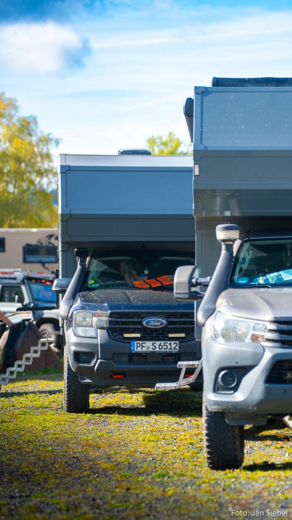 Eine Reihe von Fahrzeugen mit Wohnaufbauten auf einem Campingplatz, darunter eine Ford-Pickup mit einem besonderen Kennzeichen.